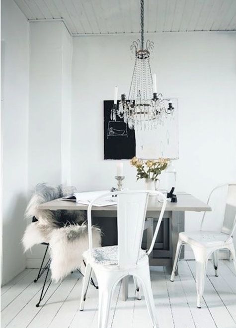 a pretty Scandinavian dining room with a table with a stone tabletop, mismatching black and white chairs, a statement artwork and a crystal chandelier