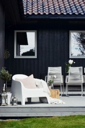 a modern Scandinavian porch with white metal chairs and a metal one with pillows, potted blooms and greenery and some candle lanterns
