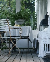 a shabby chic Scandinavian porch with metal shabby chic furniture, a white shabby daybed and neutral upholstery, greenery and a candle lantern