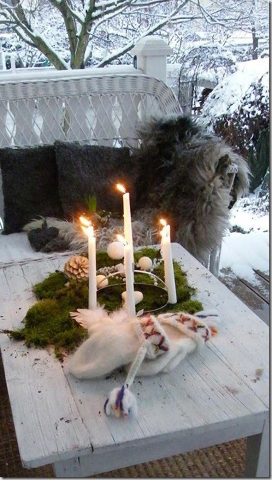 a winter Scandinavian porch with a white wicker sofa with animal skins and pillows, a whitewashed coffee table with candles and evergreens