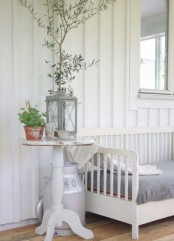 a relaxed neutral Scandinavian porch with a white daybed woth grey upholstery, a white side table, some potted plants and a candle lantern