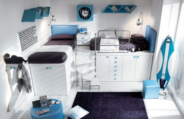 a modern shared teen boy bedroom with white walls and furniture, with beds placed on cabinets, bright blue accents