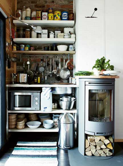 a tiny kitchen nook with open shelves, a small cooking countertop, a microwave and a wood stove next to it used as a countertop, too