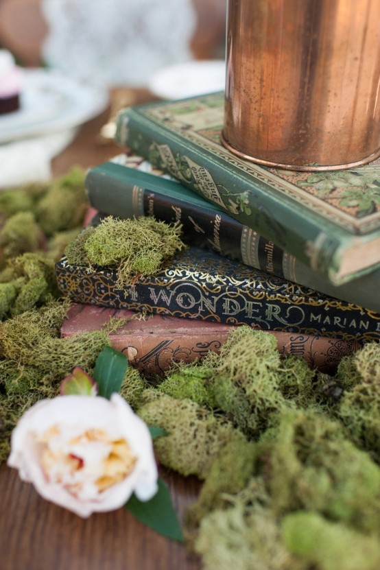 a stylish centerpiece of fairy tale books, moss and blush blooms plus some candles on top