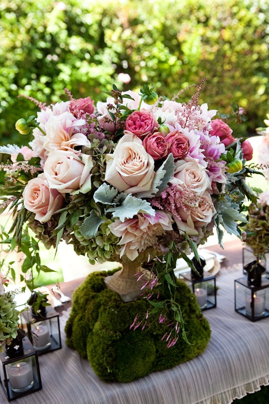 a super lush and beautiful pink floral centerpiece in a vintage urn on a cushion of moss can be used for special occasions including weddings