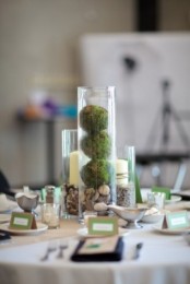 a simple centerpiece of a glass of pebbles and moss and some candles in glasses for a rustic feel