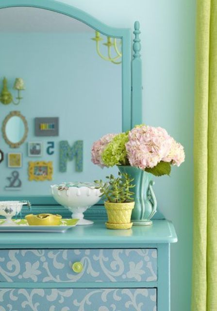 a turquoise room with a turquoise vanity with a mirror and drawers, some pretty decor and mustard-colored curtains is wow