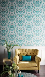 a turquoise and white wallpaper wall, a pale yellow velvet chair and a turquoise pillow, beautiful turquoise vases with blooms