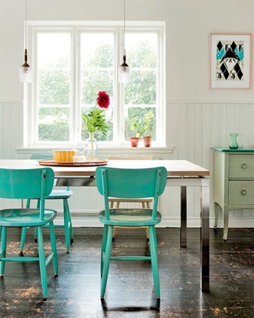 an eclectic kitchen with a neutral dining table, turquoise chairs, a green sideboard and some elegant pendant lamps