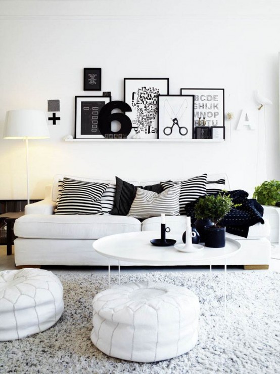 a Scandinavian living room done in black and white, with white furniture, black decor, greenery and a ledge with lots of artworks is very chic