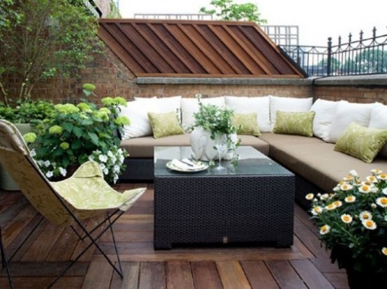 a modern rooftop terrace with an L-shaped sofa, a leather butterfly chair and potted blooms and greenery