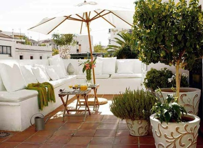a simple and modern white rooftop terrace with an L shaped sofa, an umbrella, some potted greenery feels fresh and cool