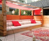 a bright modern terrace with a large wooden bench with a red canopy and red pillows plus a boho rug is a bold and cool place to be