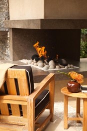 a modern terrace with an open fireplace with pebbles and simple wooden upholstered furniture is a lovely place to stay