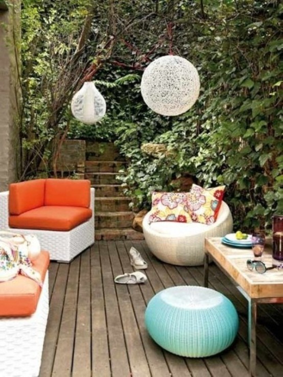 a small modern terrace with bright wicker furniture and pillows, with woven lamps, greenery all around and bright accessories
