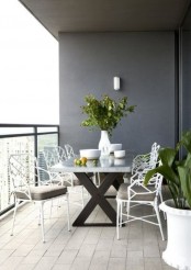 a modern balcony dining space with a trestle table and white metal chairs plus potted greenery for a fresh feel