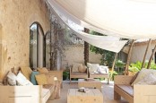 a modern terrace with light-colored wooden furniture, printed pillows and potted greenery plus curtains