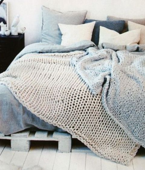 an arrangement of knit pillows and blankets in a wintry color palette make the bedroom very welcoming and super cozy