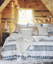 a cozy cabin winter bedroom all clad with rough wood, with lights, a pompom garland and lots of fluffy pillows