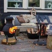 a Scandinavian terrace with a wooden deck, wooden furniture with cozy upholstery and pillows, a couple of hearths and a firewood stand