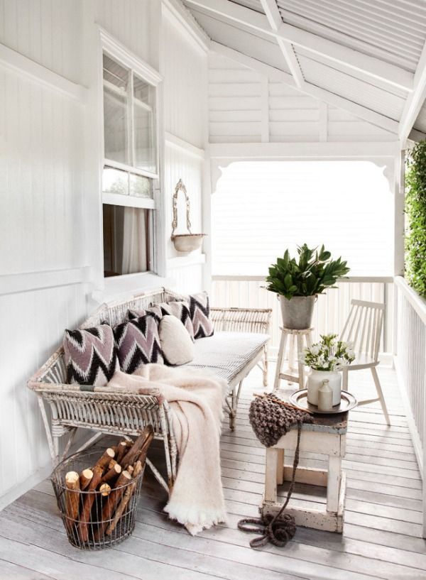 a neutral winter terrace done with a white bench, neutral upholstery and printed pillows, potted plants and vintage chairs