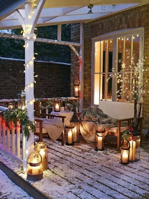 a cozy and welcoming winter terrace with wooden furniture with white upholstery, lights, lanterns and blankets and evergreens