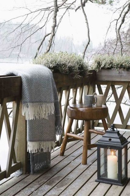 a winter deck with a lake view, blankets, potted greenery, a stool and a lantern is a lovely and relaxed space to spend time