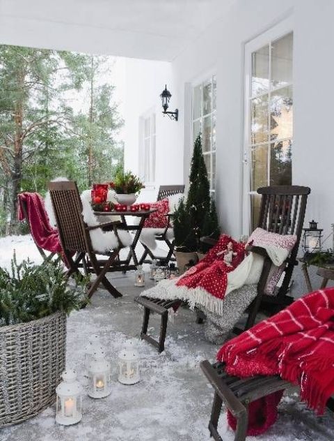 a beautiful winter or Christmas terrace with dark stained wooden furniture, red and white blankets, potted plants candle lanterns is a very cozy and lovely space