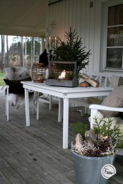 a Scandinavian terrace with a wooden deck, white garden furniture, pillows and faux fur, wovne lanterns and Christmas trees