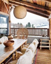 a chalet terrace with a dining zone, rustic wooden furniture and white faux fur, a peacock chair and a woven pendant lamp plus a cozy boho rug
