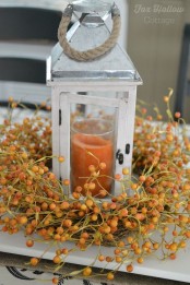 a faux berry wreath surrounding a candle lantern with an orange candle is a lovely and easy rustic centerpiece for the fall