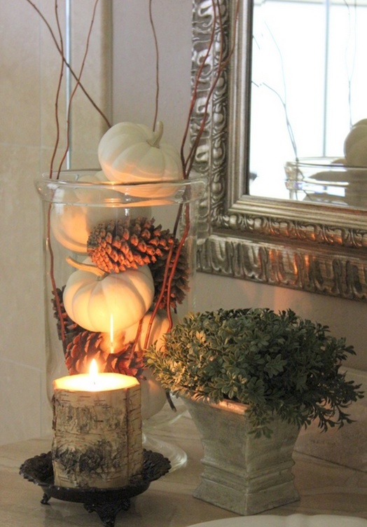 a tall vase with pinecones and pumpkins, with twigs and a candle wrapped with bark for a cool rustic arrangement
