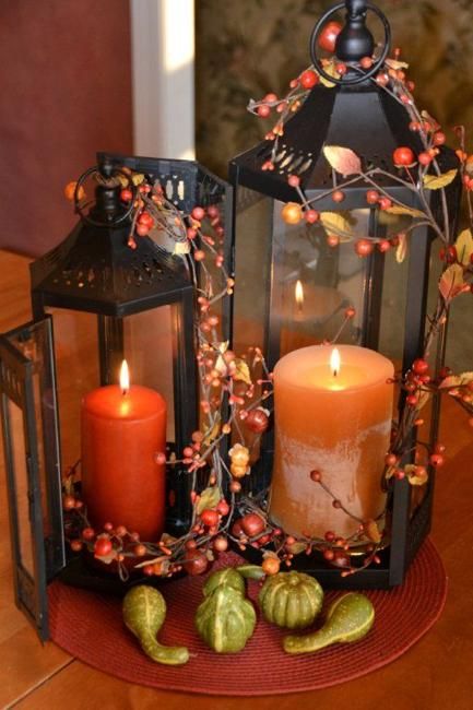 rust and orange candles in candle lanterns wrapped wiht berries and with gourds and pumpkins around