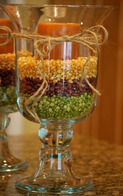 a glass candleholder filled with peas, beans and corn and with a bright pillar candle on top is a bright and rustic fall decoration