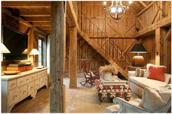 a real barn living room clad with wood, with wooden beams and pillars, neutral seating furniture, a large white sideboard and printed and colorful textiles
