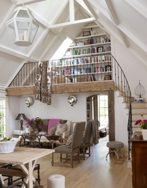 a neutral barn living room with a wooden beam and pillar, with neutral seating furniture, a trestle dining table and a reading nook with lots of built-in bookshelves