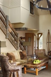 a barn living room with white planked walls, neutral seating furniture, a low coffee table, a large chandelier and reclaimed wood railing is chic and welcoming