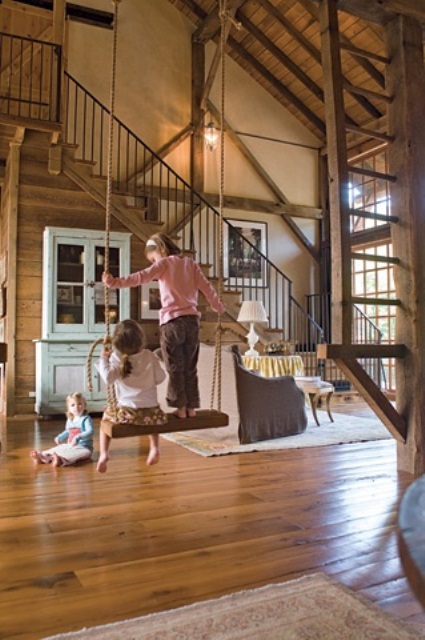 a vintage barn living room clad with wood, with wooden stairs, a swing, neutral and pastel vintage furniture and lots of natural light