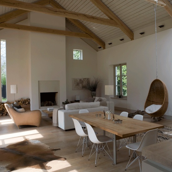 a neutral contemporary barn living room with a sleek fireplace, white seating furniture, a pendant chair, a sleek contemporary dining zone