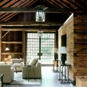 a barn living room with wooden walls and a ceiling, with wooden beams and a fireplace clad with wood, with white furniture, pendant and table lamps is a very fresh and cool idea