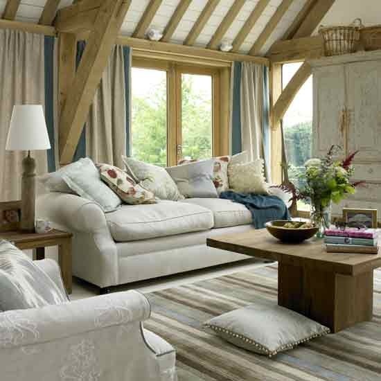 a vintage neutral barn living room with wooden beams and pillars, with white seating furniture, a wooden coffee table, baskets and printed textiles
