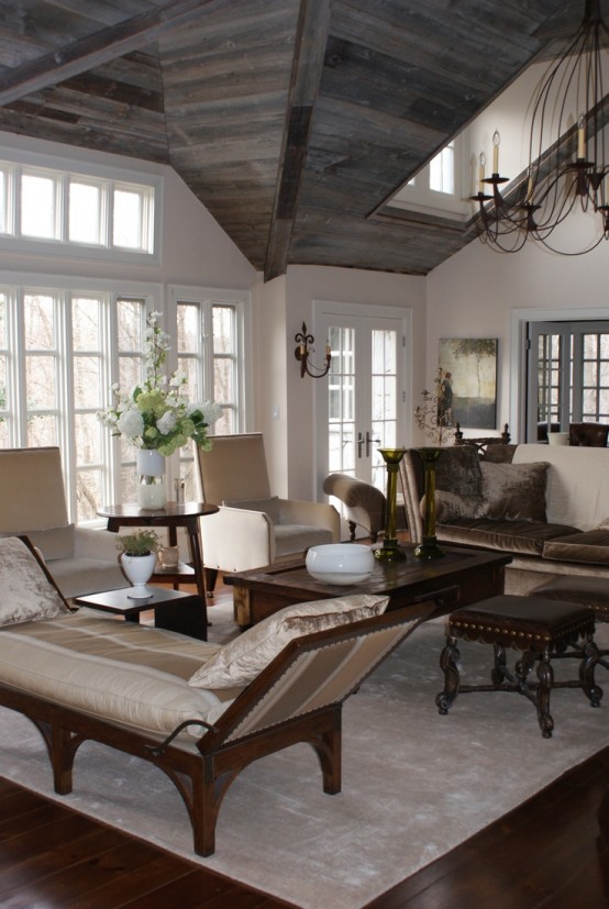 a refined barn living room with a reclaimed wood ceiling, white walls, a vintage chandelier, neutral printed furniture with dark stained legs is amazing