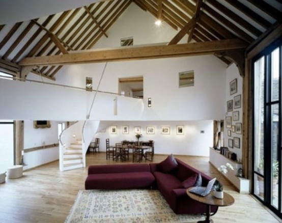 a barn living room with wooden beams and pillars, with a purple sectional, a round coffee table and a printed rug is very welcoming and light-filled