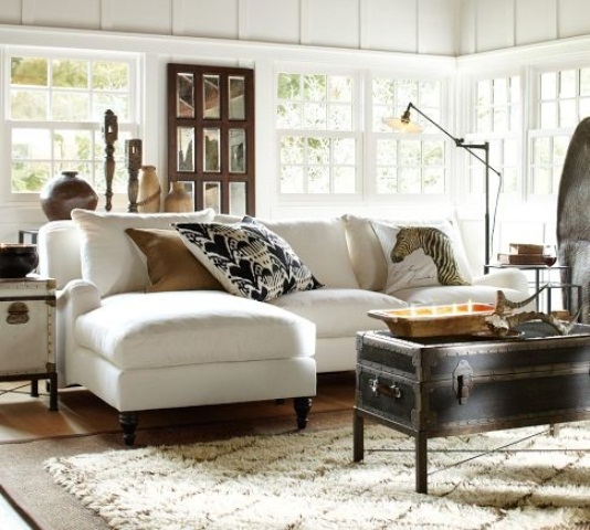 a white barn living roomw ith multiple windows, a white sectional, a black chest as a coffee table, a mirror in a dark frame and dark candleholders