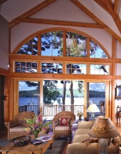 a barn living room with wooden beams and pillars, with a gorgeous view, neutral seating furniture and table lamps plus bright blooms