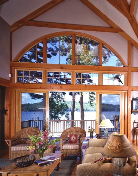 a barn living room with wooden beams and pillars, with a gorgeous view, neutral seating furniture and table lamps plus bright blooms