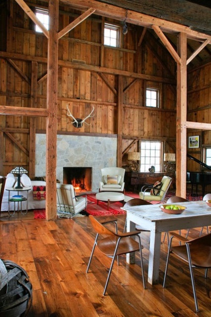 a modern barn living room fully clad with wood, with wooden pillars and beams, a fireplace clad with stone, neutral seating furniture, a dining zone here