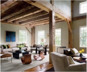 a barn living room with wooden beams and pillars, with chic contemporary furniture, neutral and dark, with low coffee tables and a bold artwork is amazing