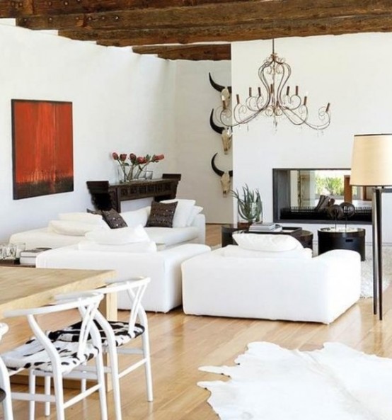a pretty barn-inspired modern living room with a double-sided fireplace, white seating furniture, a dark console and dark tables for a contrast