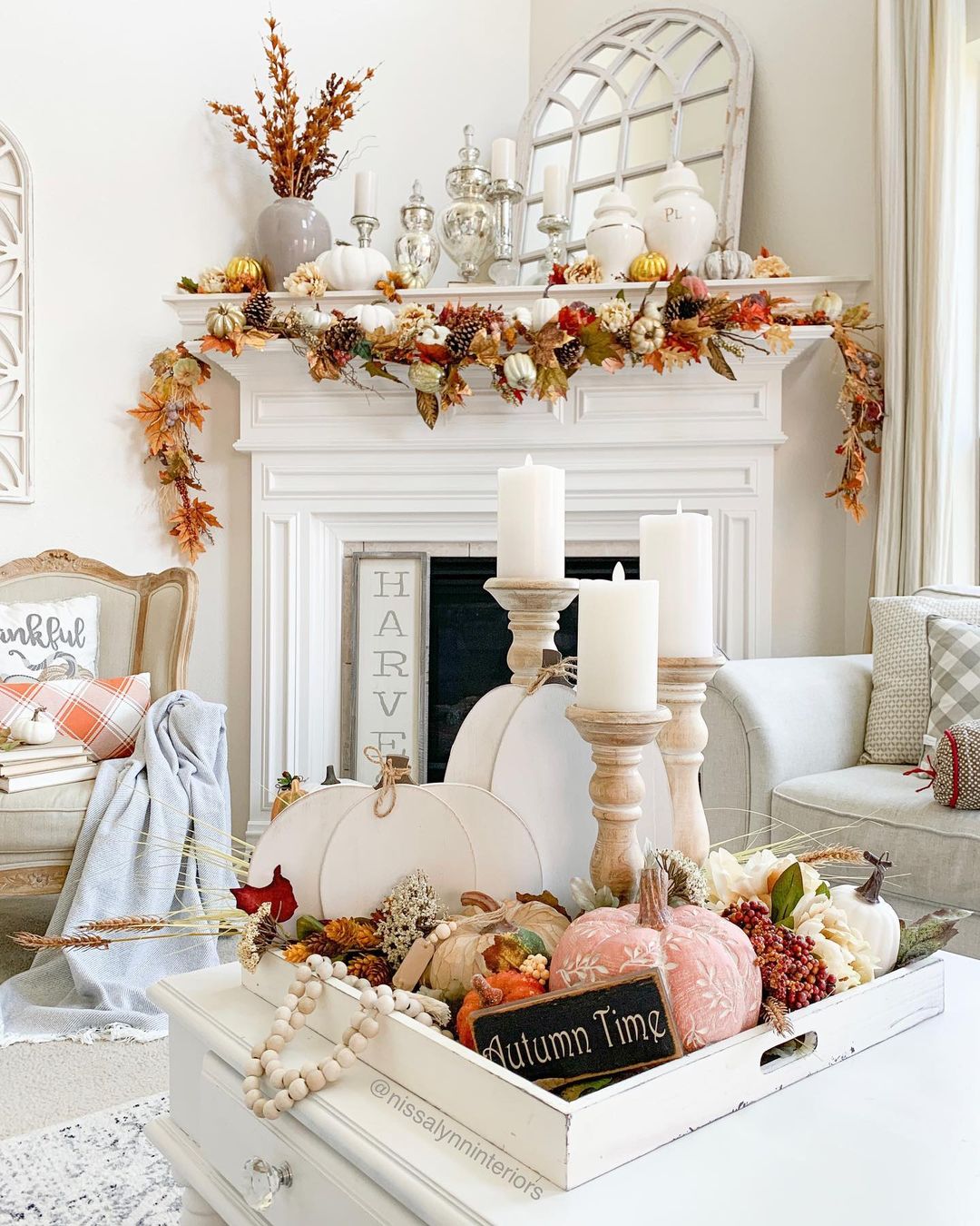 a rust-colored pillow and blanket plus dried branches arrangements in vases add a fall touch to the space